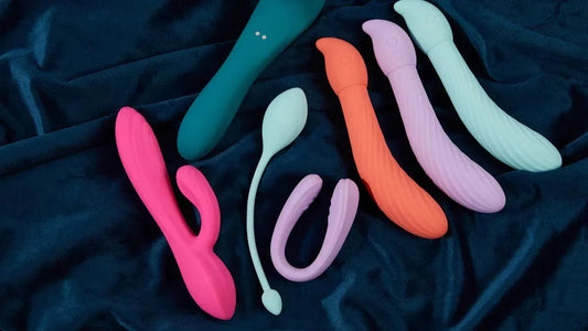 Colorful vibrators and adult toys on dark fabric, including G-spot and clitoral designs for pleasure.