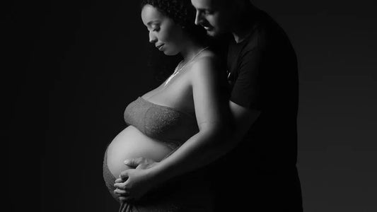 Pregnant woman in sparkling strapless top, embraced by partner, black and white studio portrait