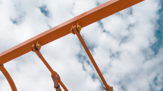 Hands gripping orange playground bars under cloudy sky
