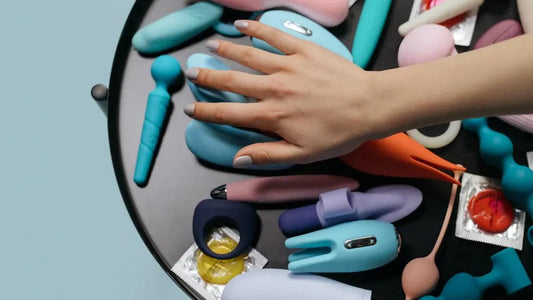 Hand selecting colorful adult toys and vibrators on a black tray with condoms nearby