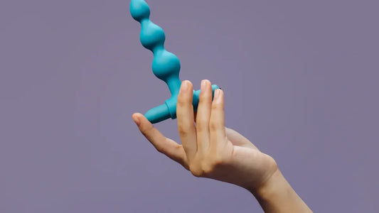 Teal silicone wand vibrator with bulbous nodes, held in hand against purple background