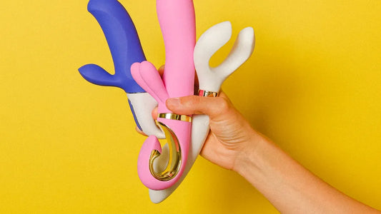 Hand holding colorful vibrators with gold accents against yellow background