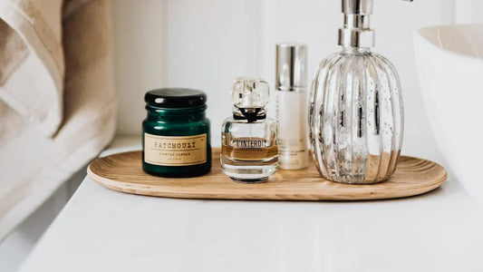 Patchouli scented candle, L'Interdit perfume, and luxury bathroom accessories on wooden tray